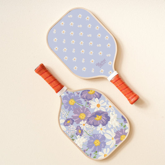 The-darling-effect’s Bouquet Beauty Purple Pickleball Paddle, with orange handles and floral designs, is displayed on a light surface—perfect for your next pickleball game.