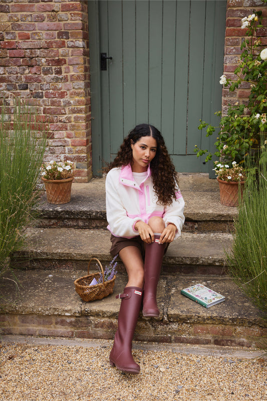Model wearing Gym+Coffee Snap Polar Fleece Pink Blossom seated on garden steps Shop Gym+Coffee at Dotique